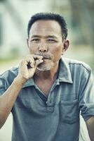 stänga upp ansikte av asiatisk senior man med torr löv cigarett ser till kamera foto