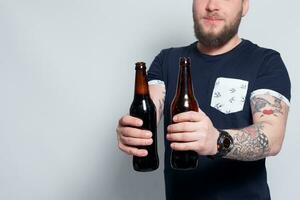 Brutal skäggig manlig med tatuerade ärm drycker en öl från en flaska. foto