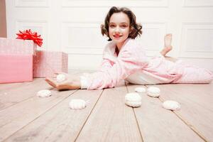 söt liten flicka i pyjamas med sötsaker Sammanträde på de golv foto