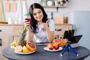 attraktiv, atletisk, leende, ung kvinna som äter hälsosamt och förbereder fruktsmoothies foto