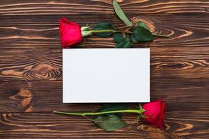 röda rosor och tomt papper på träskiva, alla hjärtans dag bakgrund, bröllopsdag foto
