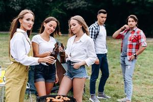 ett sällskap av vänner som höjer en flaska med en öl på campingen. - horisontell bild foto