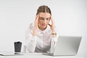 trött affärskvinna som sitter bakom en bärbar dator med en kopp kaffe och ipad på bordet och rör vid hennes huvud för händer foto
