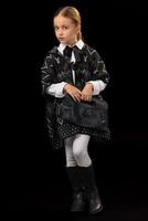 liten flicka i en mörk poncho, svart stövlar och en koppling i henne hand foto