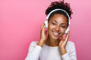 porträtt av en vacker flicka i hörlurar som lyssnar på musik över rosa bakgrund - bild foto