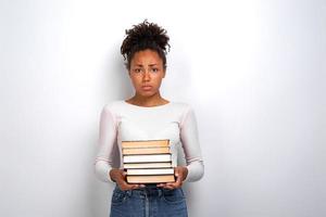 ledsen olycklig ung flicka som håller böcker som står i studio vit bakgrund. tillbaka till skolan foto