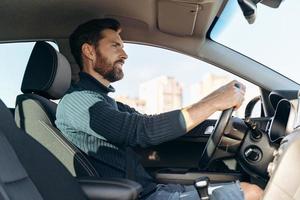 lågvinkelsikt över den seriösa självsäkra mannen som kör på bilen och tittar på vägen under körning. lager foto