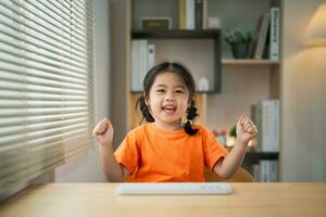 asiatisk bebis flicka bär t-shirt leende glad Lycklig använda sig av bärbar dator och studie uppkopplad på trä tabell skrivbord i levande rum på Hem. utbildning inlärning uppkopplad från Hem begrepp. foto