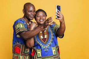 glad man och kvinna par innehav smartphone, ser på främre kamera och tar selfie. leende fru och Make med sorglös uttryck Framställ tillsammans och framställning Foto på mobil telefon