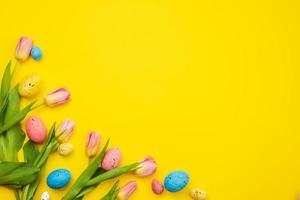 tulpaner och färgglada ägg ligger i hörnet på gul påskbakgrund, tomt copyspace foto