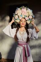 brunett flicka i en vit ukrainska äkta nationell kostym och en krans av blommor är Framställ mot en vit hydda. närbild. foto
