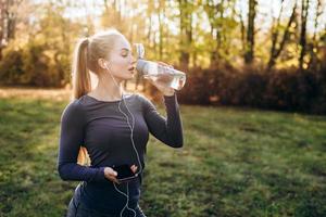 en ung, vacker flicka i hörlurar dricker vatten efter ett träningspass. foto