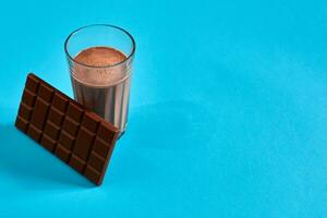 glas av choklad mjölk med choklad bar på blå bakgrund med Plats för text eller design foto