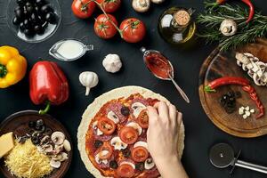 händer av bagare tillsats Ingredienser in i pizza under pizza förberedelse på kök foto