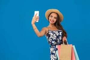 ung eleganta kvinna Framställ och tar en selfie på de telefon med handla påsar på en blå bakgrund foto