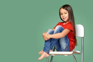 liten flicka bär röd t-kort och Framställ på stol foto