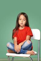 liten flicka bär röd t-kort och Framställ på stol foto