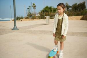 barn flicka eftertänksamt drömmande ser in i de distans, stående på henne blå skridsko styrelse på ett ben på skridsko parkera foto