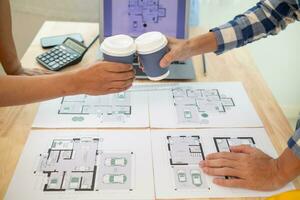 lag ingenjörer, arkitekter och verklig egendom investerare karnade över kopp av varm kaffe till gratulera dem deras framgångsrik projekt design inom budget. varm kaffe krock begrepp till fira i kontor foto