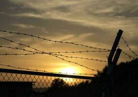 silhuett av hullingförsedda tråd staket på solnedgång foto