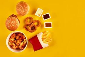 snabb mat maträtt topp se. franska pommes frites, hamburgare, majonnäs och ketchup såser på gul bakgrund. foto