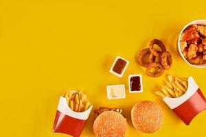 snabb mat maträtt topp se. kött hamburgare, potatis pommes frites och kilar. ta bort sammansättning. franska pommes frites, hamburgare, majonnäs och ketchup såser på gul bakgrund. foto