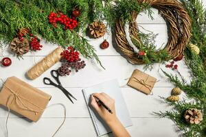 topp se av kvinna händer slå in ny år närvarande. packade gåvor och rullar, gran grenar och verktyg på trä- tabell. foto