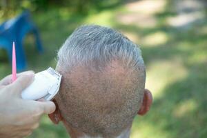 ett äldre asiatisk person får hans hår skära utomhus. foto