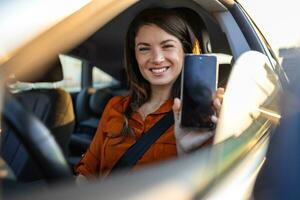 bil hyra app. Lycklig kvinna som visar tom smartphone medan Sammanträde inuti av bil, leende kvinna demonstrera kopia Plats för mobil annons eller hemsida, attrapp foto