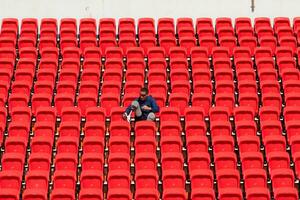 Inaktiverad idrottare i en blå skjorta Sammanträde på de röd säten på de stadion, förbereda för löpning Träning. foto