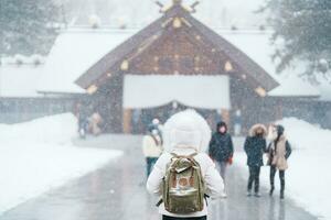 kvinna turist besöker i sapporo, resande i Tröja ser hokkaido helgedom med snö i vinter- säsong. landmärke och populär för attraktioner i Hokkaido, japan. resa och semester begrepp foto