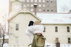 kvinna turist besöker i sapporo, resande i Tröja sightseeing sapporo klocka torn med snö i vinter. landmärke och populär för attraktioner i Hokkaido, japan. resa och semester begrepp foto
