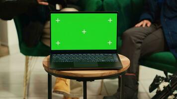 digital enhet med grönskärm mall placerad på kaffe tabell i vardagsrum område på lyx alpina åka skidor tillflykt. människor Sammanträde på soffa chattar, bärbar dator löpning isolerat copy visa på hotell. foto