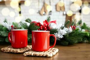 två röd muggar på trä- tabell med jul dekorationer med bokeh lampor effekt på bakgrund foto