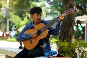 asiatisk pojke lyckligt sitter utanför spelar gitarr med hans läger vänner under ha sönder. mjuk och selektiv fokus. foto