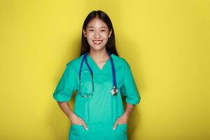 porträtt av en skön ung kvinna i en gul bakgrund, asiatisk kvinna bär en läkares enhetlig gör en leende uttryck, en ung kvinna bär en medicinsk stetoskop har en vänlig uttryck. foto