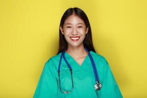 porträtt av en skön ung kvinna i en gul bakgrund, asiatisk kvinna bär en läkares enhetlig gör en leende uttryck, en ung kvinna bär en medicinsk stetoskop har en vänlig uttryck. foto