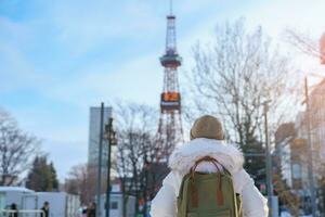 kvinna turist besöker i sapporo, resande i Tröja sightseeing sapporo torn med snö i vinter. landmärke och populär för attraktioner i Hokkaido, japan. resa och semester begrepp foto