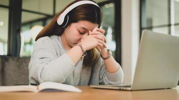ung asiatisk tjej håller händerna och huvudet ner trött uttryck medan du studerar online med laptop.