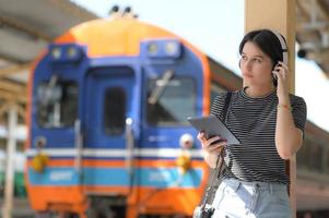 en tonårskvinna som bär hörlurar och lyssnar på musik från en app på en surfplatta i väntan på ett tåg foto