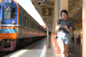 en tonårskvinna som bär hörlurar och lyssnar på musik från en app på surfplattan medan hon väntar på ett tåg ..