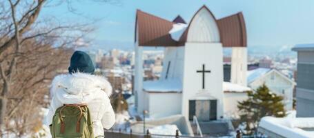 kvinna turist besöker i hakodate, resande i Tröja sightseeing biskops- kyrka med snö i vinter. landmärke och populär för attraktioner i Hokkaido, japan. resa och semester begrepp foto