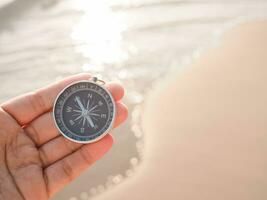 stänga upp hand innehav kompass med strand bakgrund foto