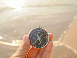 stänga upp hand innehav kompass med strand bakgrund foto