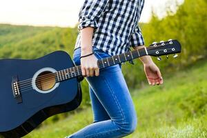 flicka gående i de fält med en gitarr i hand foto