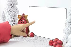 de finger är pekande på tapelet med en vit skärm mock-up och vit kalender med en festlig scen av en skön jul träd Utsmyckad, med jul bollar, tall kottar, och en röd hus gåva låda. foto