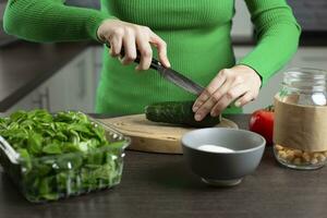 kvinna nedskärningar gurka för matlagning vegetabiliska sallad. Hem kök. foto