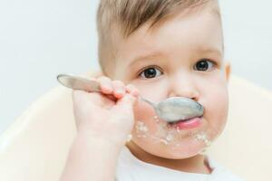 förtjusande bebis pojke äter gröt med en små sked han själv foto
