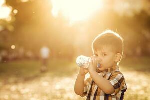 stilig pojke drycker klar vatten från en flaska på en solig dag utanför foto