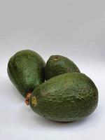 tre färska avokado med hud på den vita ytan, avokado av naturligt ursprung för att förbereda vegetarisk mat foto